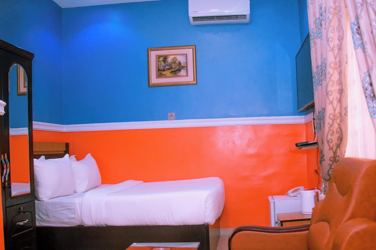 Une pièce comprenant un lit, une chaise, un bureau avec un téléphone et un tableau accroché au mur.