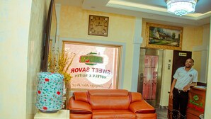 A lobby with a clock, a framed painting, a sofa, and a sign for Sweet Savors. - Sweet Savor Hotels and Suites Annex (Lagos)
