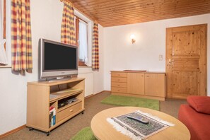 Une pièce avec un téléviseur posé sur un meuble en bois, un canapé rouge, une armoire en bois et une porte.