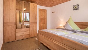 Ein Schlafzimmer mit einem Holzkleiderschrank, einem Bett mit Kissen, einem Nachttisch und einem an der Wand hängenden Bild.