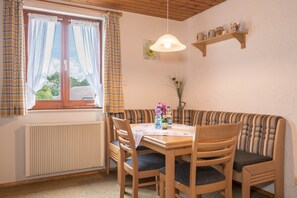 Un coin repas avec une table ronde, des chaises en bois, un banc, un radiateur, une fenêtre avec des rideaux et un luminaire suspendu.