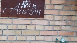 Eine Ziegelwand mit einem Schild, auf dem 'Auszeit' steht, und einem darunterliegenden Schild mit der Aufschrift 'WILLKOMMEN'.