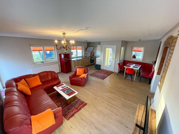 A modern living room with a red sofa, a dining area with red chairs, and a kitchen with a red refrigerator.