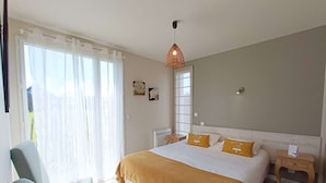 Ein Schlafzimmer mit einem Bett, einem Sessel, einem Nachttisch, einem Fenster mit Vorhängen und einer Pendelleuchte.