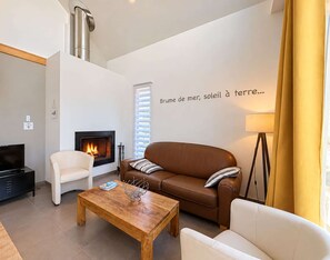 A modern living room with a fireplace, a sofa, a coffee table, and a wall with a French quote.