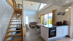 Eine moderne Küche mit integrierter Kochinsel, ein Essbereich mit einer Couch und eine Treppe, die zu einer oberen Ebene führt.