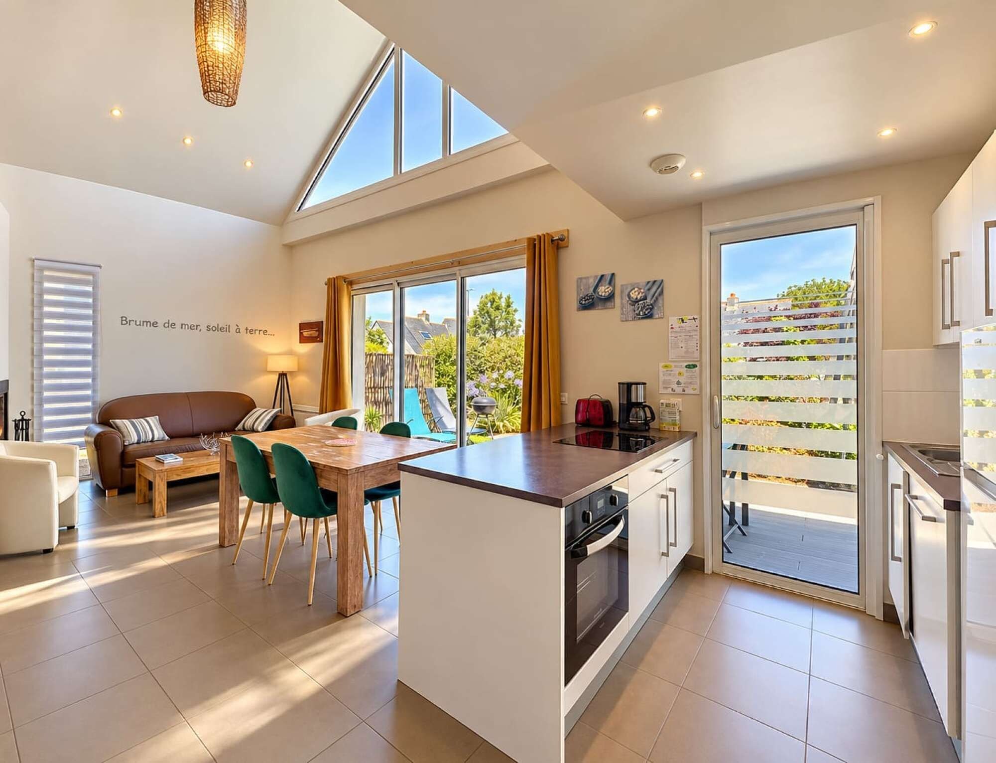 A modern kitchen with a large island, a dining area with a sofa and chairs, and a view of a garden through the windows.