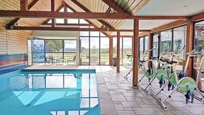 Ein überdachter Pool mit Ergobikes und eine Terrasse mit Sitzgelegenheiten im Freien.