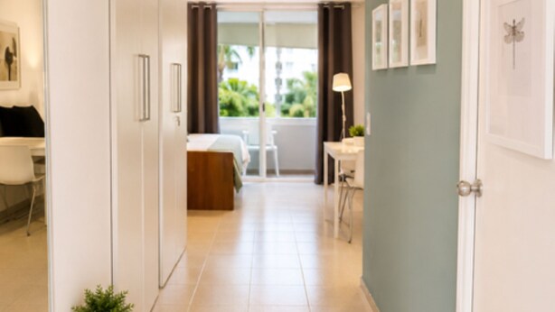 A modern hallway with a bed, a desk, and a plant.