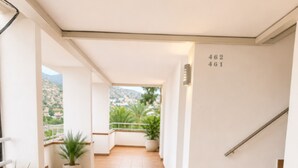 A corridor with tiled flooring, potted plants, a staircase, and a view of a hillside.