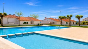A rectangular swimming pool with steps leading into it, surrounded by a paved area with buildings in the background.