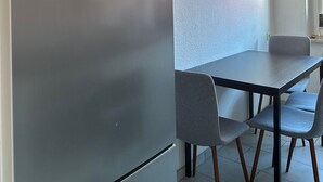 Une cuisine moderne équipée d’un réfrigérateur en acier inoxydable, d’une table à manger avec quatre chaises et d’une fenêtre laissant entrer la lumière naturelle.