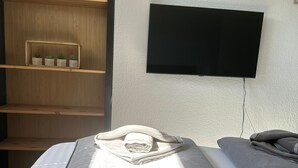 Une chambre à coucher comprenant un lit, une table de chevet avec un téléphone, un téléviseur fixé au mur et une armoire en bois avec des étagères.