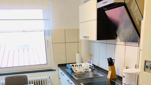 Une cuisine moderne avec un plan de travail noir, des meubles blancs et une fenêtre équipée de stores.