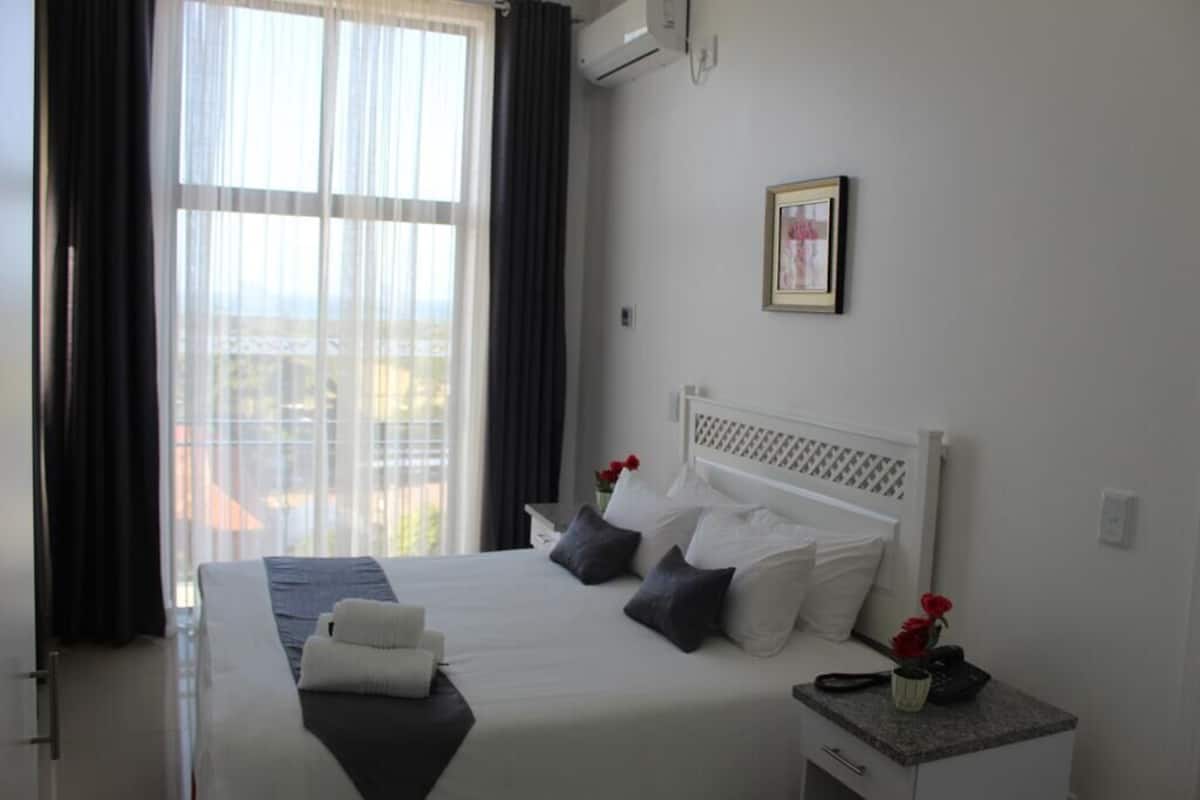 A hotel room with a large bed, a bedside table with a phone and vase, and a window with curtains.