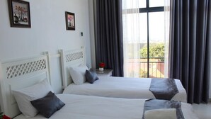 Une chambre d’hôtel avec deux lits, des têtes de lit blanches et un balcon avec vue.