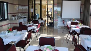 Une salle de conférence avec des tables disposées pour une réunion, un écran de projection et une vue sur l’extérieur.