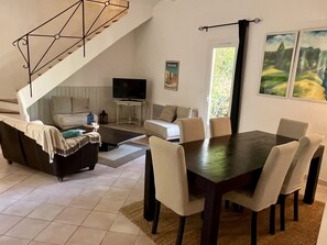 A modern living room with a dining table, sofas, a TV, and a staircase.