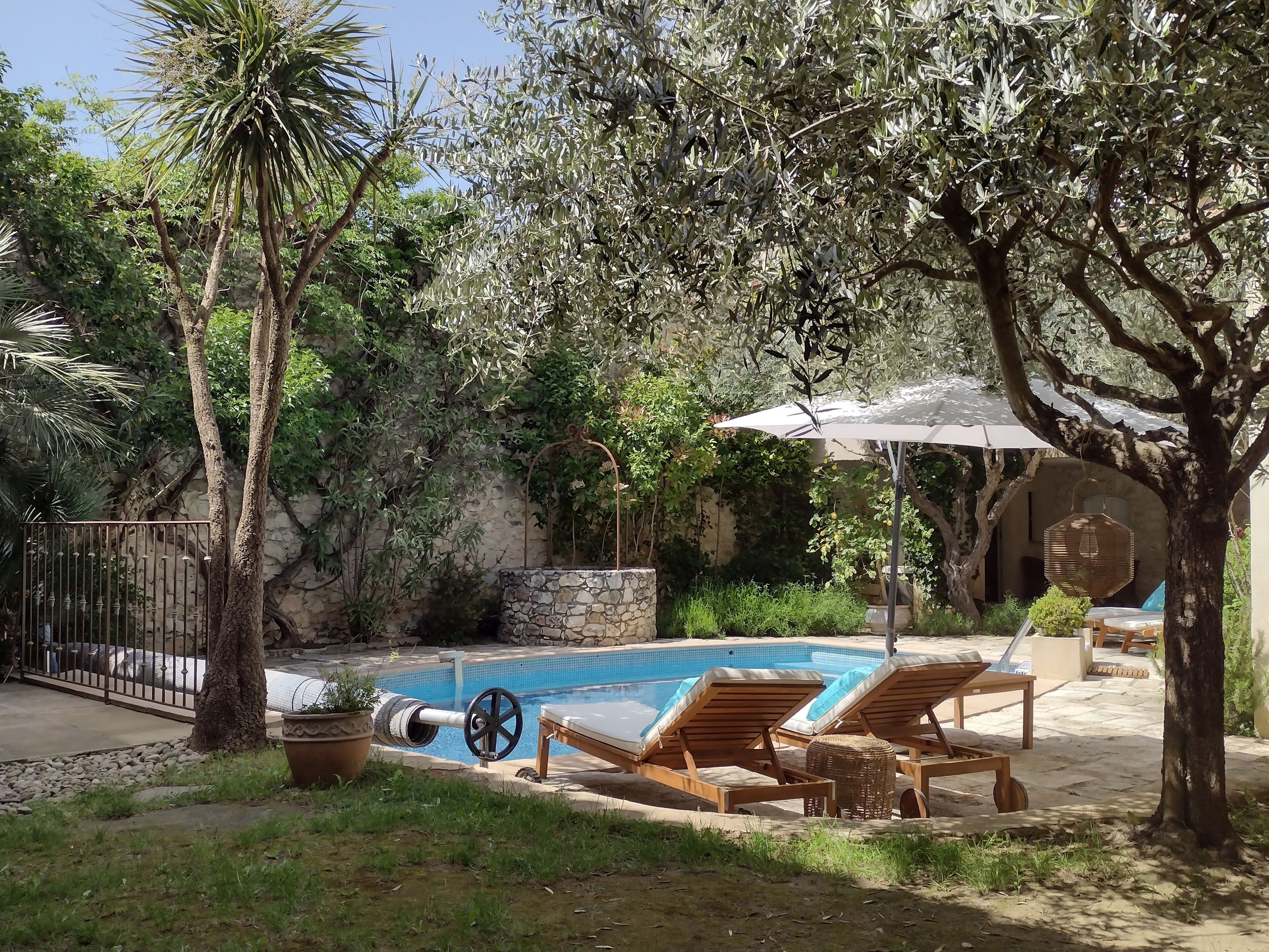 Area piscina con lettini e ombrellone, circondata da alberi e un muro di pietra.