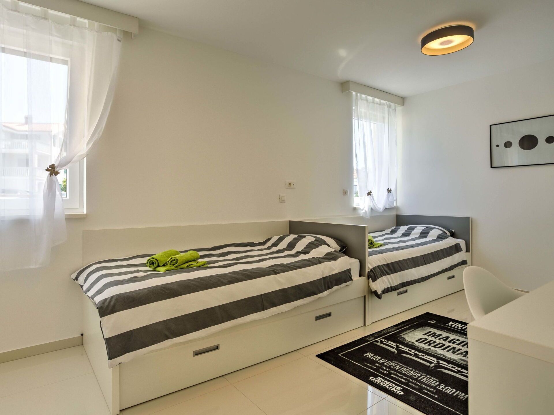 Une chambre d’hôtel moderne avec deux lits, un grand miroir et une fenêtre ornée de rideaux légers.