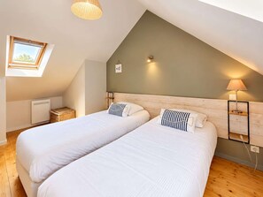 Een kamer met twee bedden, een dakraam, een wandlamp en een klein tafeltje.