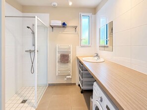Een moderne badkamer met een douchecabine van glas, een wastafel met houten blad, een handdoekhouder en een raam.
