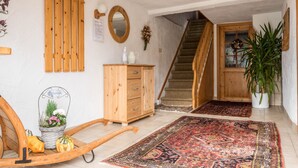 Een gang met een houten bank, een houten kast, een spiegel, een trap en een potplant.