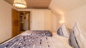 Een slaapkamer met een bed, kussens, een houten plafond en een deur die naar een andere kamer leidt.