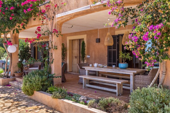 An outdoor patio with a wooden table and chairs, surrounded by potted plants and flowers.