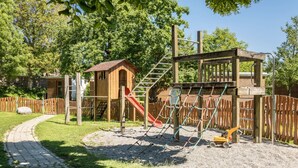 Un parque infantil con un tobogán, estructuras para escalar y un pequeño edificio de madera.