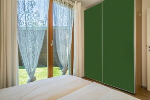 Ein Schlafzimmer mit einem Bett, einem grünen Kleiderschrank und einer Glastür, die in einen Garten führt.