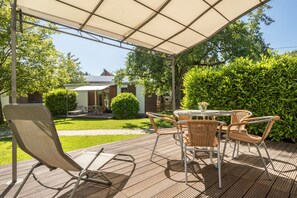 Eine Terrasse im Freien mit Tisch und Stühlen, einem Sonnenschirm und Blick auf ein Haus und Grünflächen.