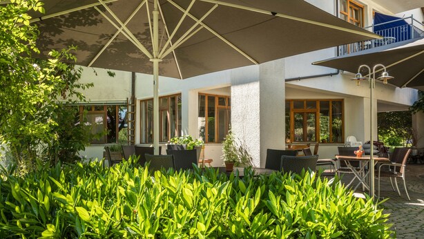 An outdoor seating area with tables and chairs, surrounded by greenery.