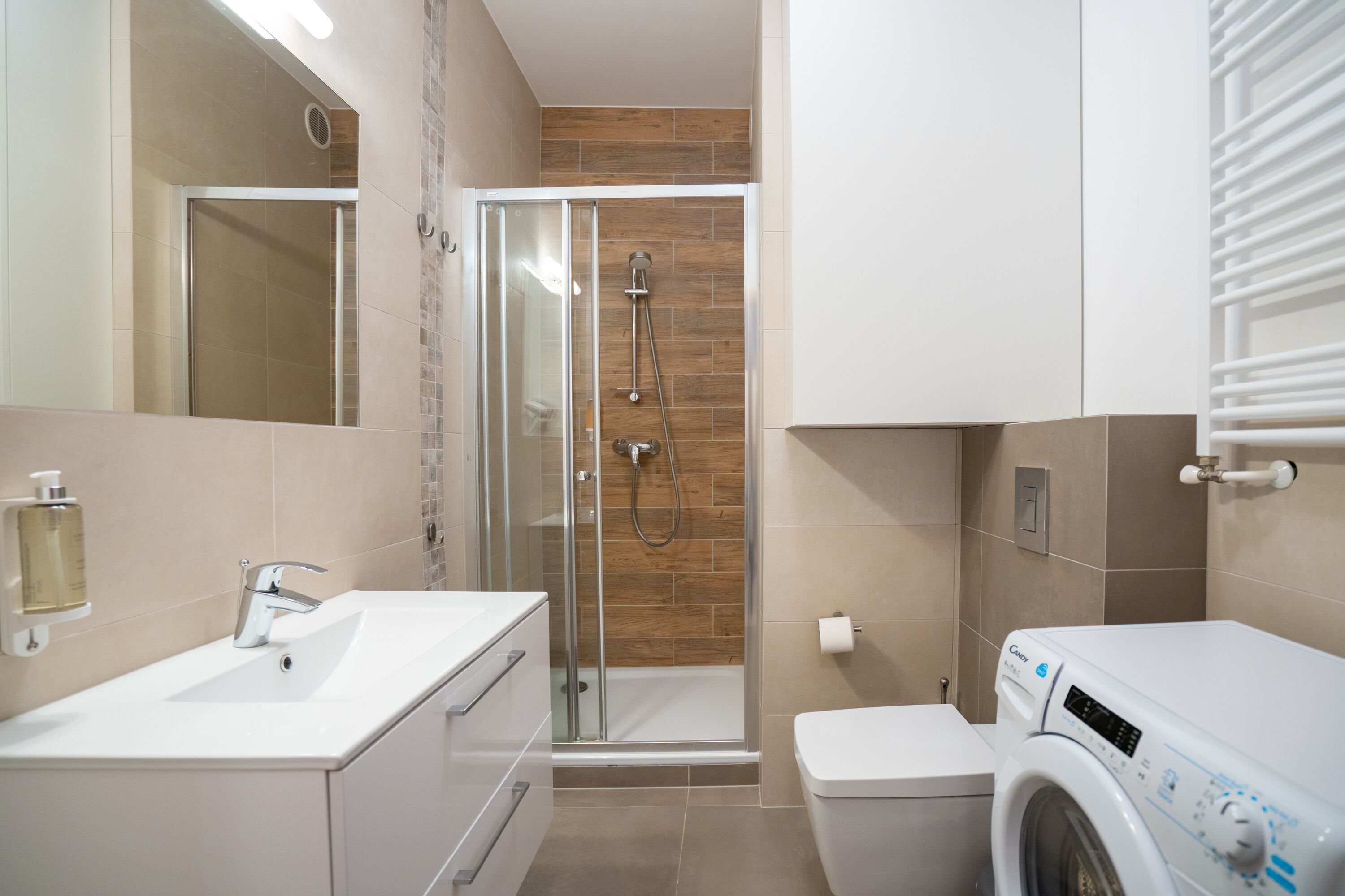 A modern bathroom with a glass-enclosed shower, a white sink, and a washing machine.