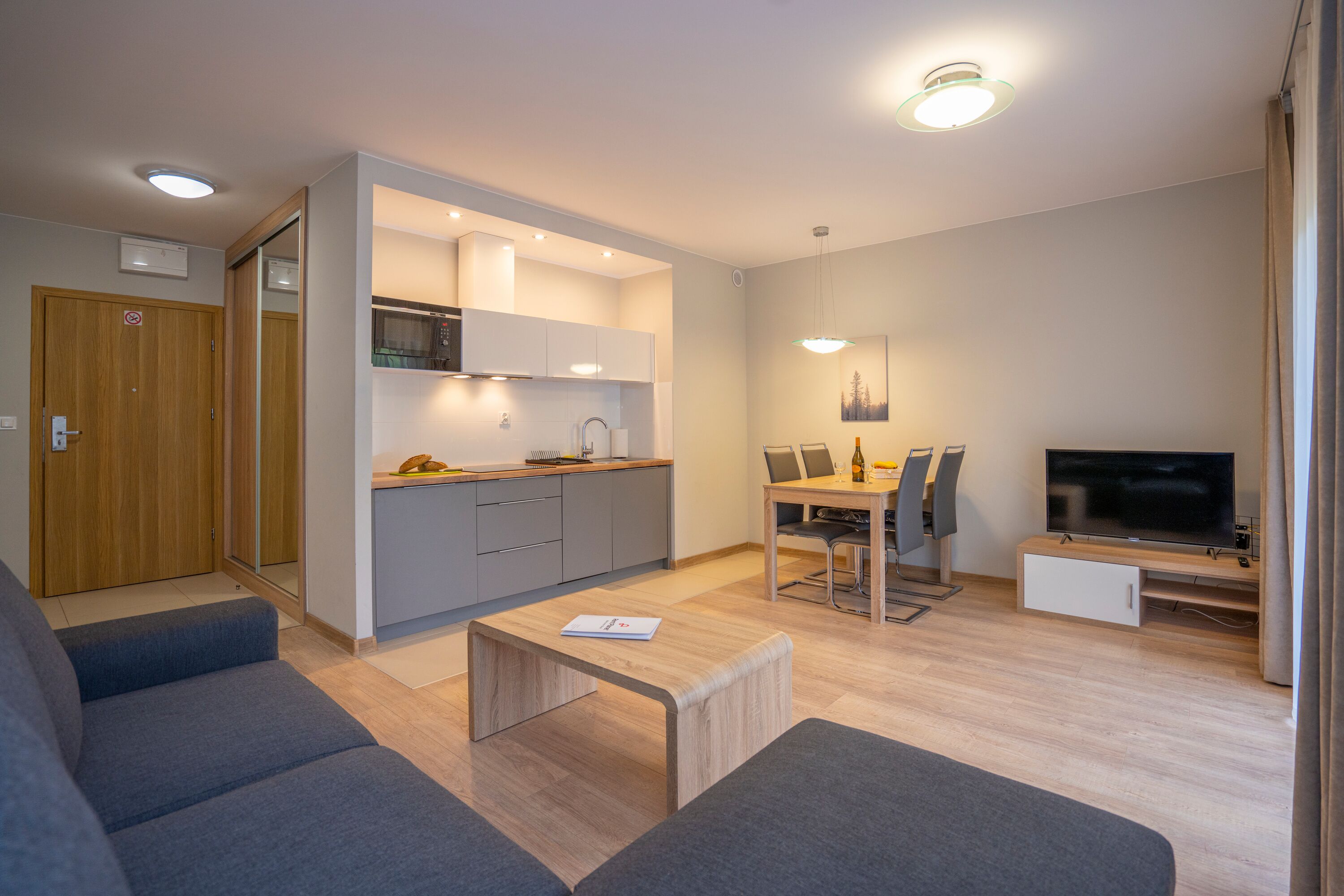 A modern living room with a sofa, a coffee table, a TV, and a dining area with chairs and a table.