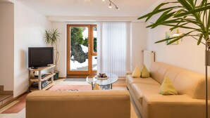 Un salon comprenant un canapé, une table basse, un téléviseur posé sur un meuble, une plante et une porte-fenêtre coulissante.