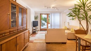 Un salon comprenant un meuble en bois, un téléviseur, un canapé, une table à manger et une grande plante.