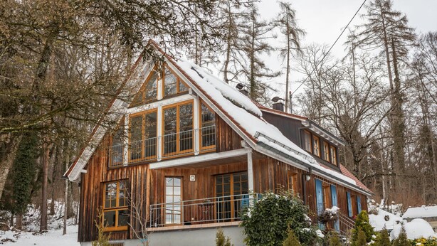 Une cabane en bois dotée d’un balcon, entourée d’arbres et de neige.