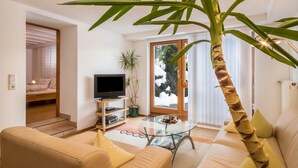 Un salon avec un canapé, une table basse, un téléviseur et une grande plante.