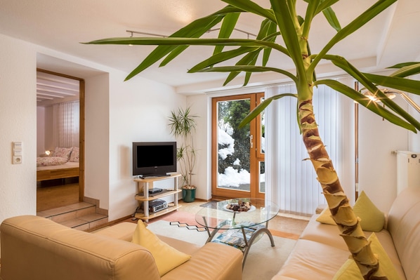 Un salon avec un canapé, une table basse, un téléviseur et une grande plante.