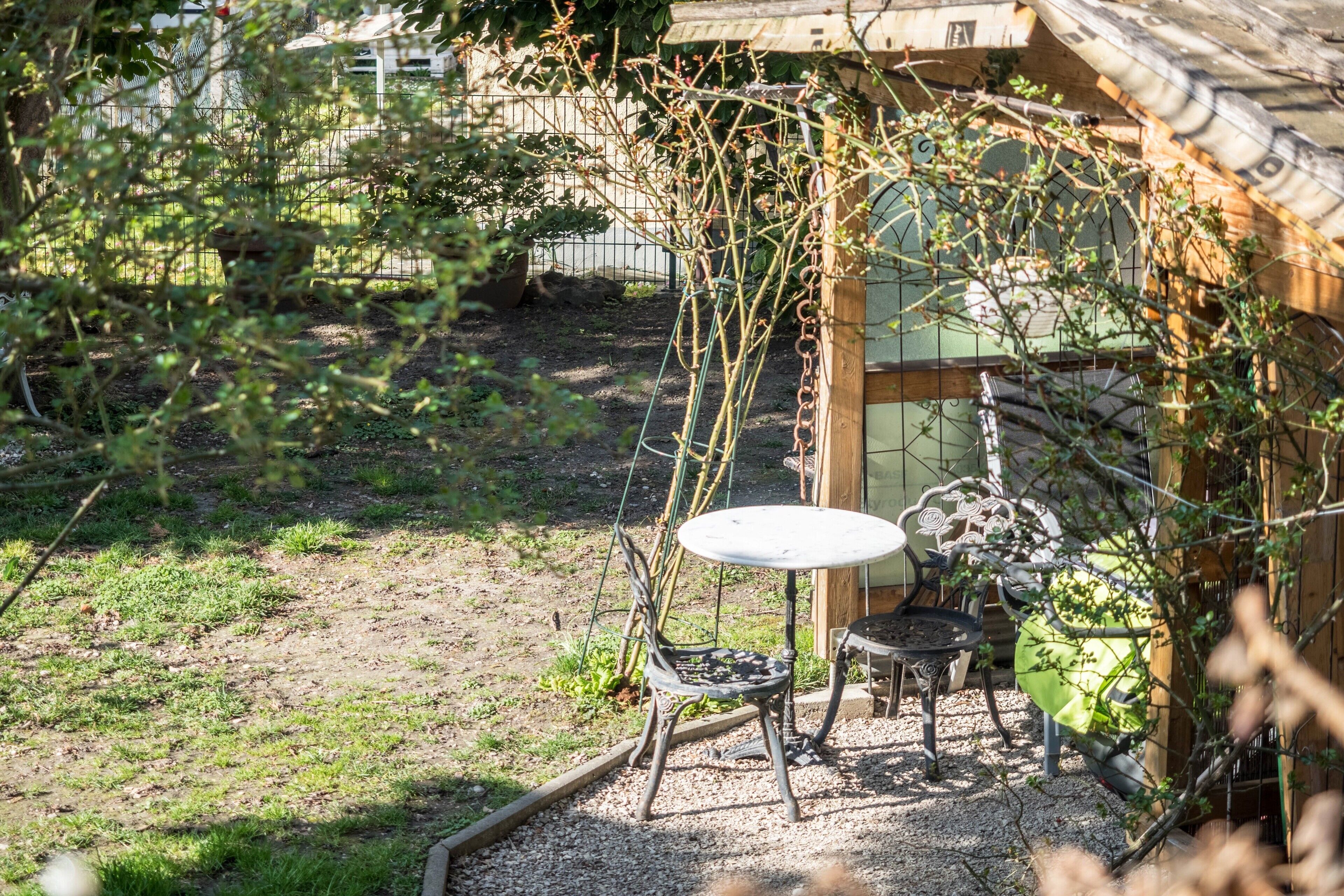 Une terrasse de jardin avec une table et des chaises, entourée de plantes et d’une clôture en bois.