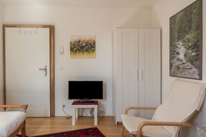 A room with a bed, a TV on a stand, a chair, a wardrobe, and a painting on the wall.