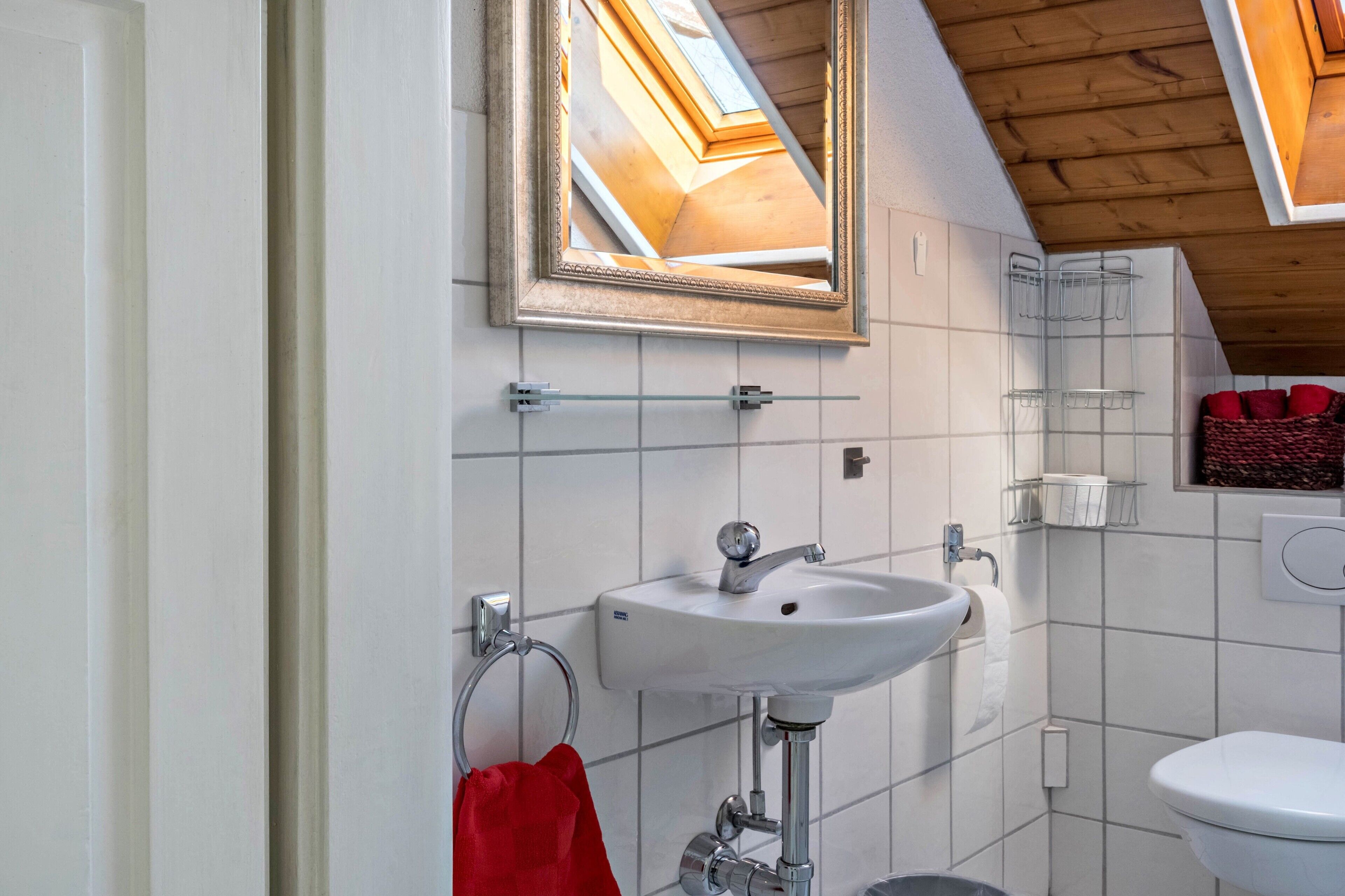 A bathroom with a skylight, white tiles, a sink, a toilet, and a red towel.