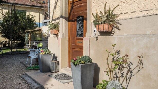 A building entrance with a wooden door, potted plants, and a small outdoor seating area.