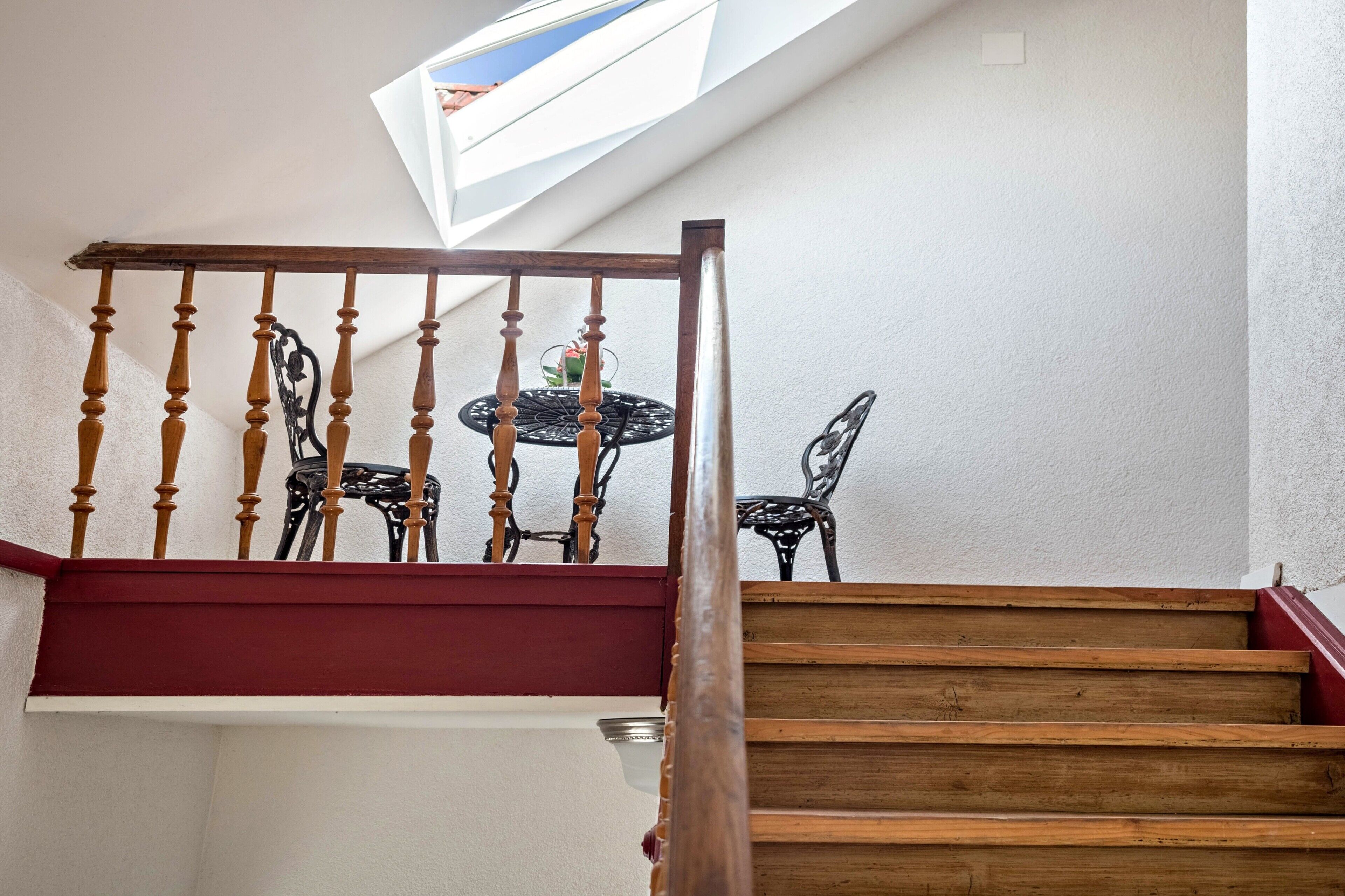 A wooden staircase with a red handrail leading to a balcony with a table and chairs.