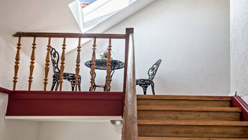 A wooden staircase with a red handrail leading to a balcony with a table and chairs.