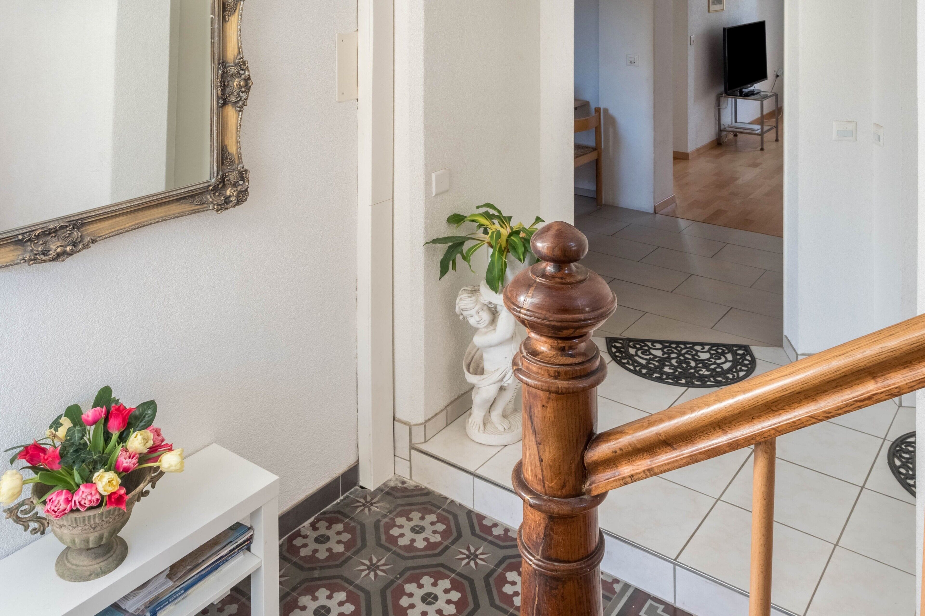 A staircase with a wooden handrail, a white console table with a vase of flowers, a decorative mirror, and a statue.