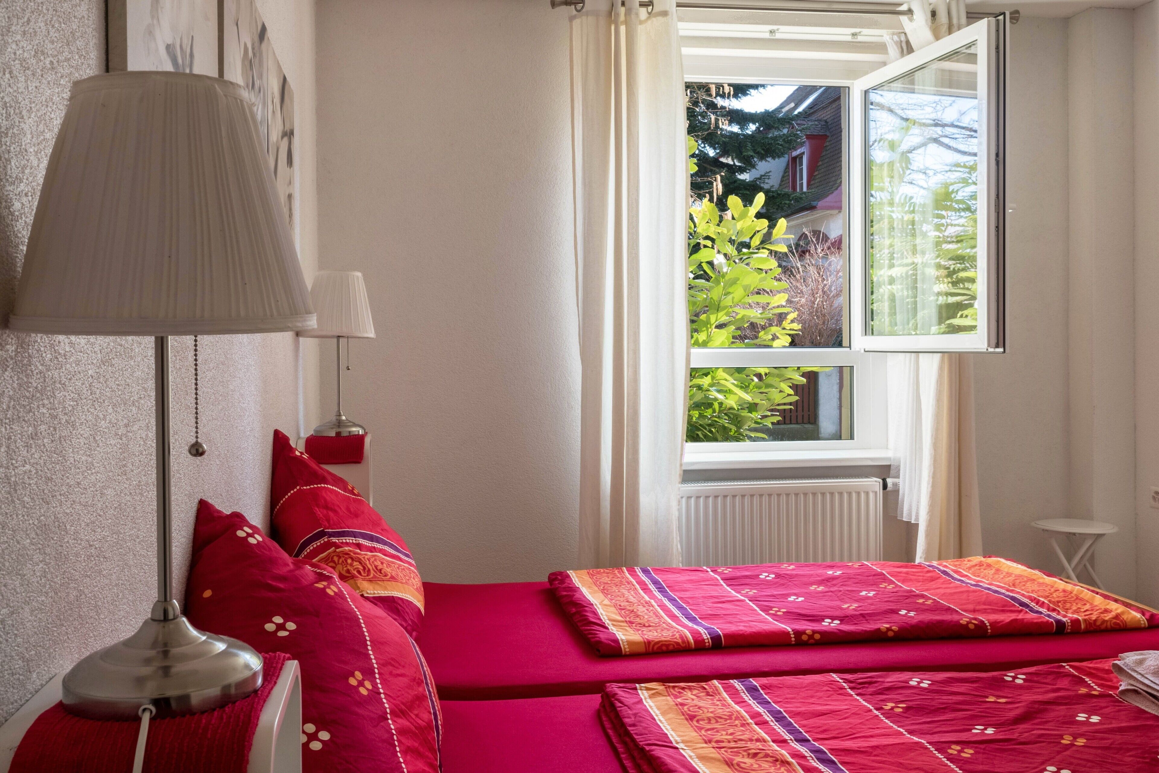 Ein Zimmer mit Bett, Lampe und Fenster mit Blick auf Grünflächen.