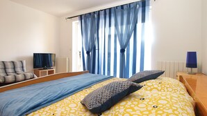 Ein Schlafzimmer mit Bett, Fernseher, Nachttisch und einem Fenster mit Vorhängen.