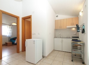 A compact kitchen with a refrigerator, wooden cabinets, and a metal rack for utensils.